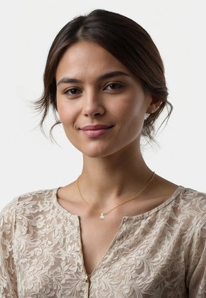 Guldhalskæde med en lille perlevedhæng, båret af en model iført en lys, gennemsigtig, broderet blomstret bluse. Neutral baggrund.