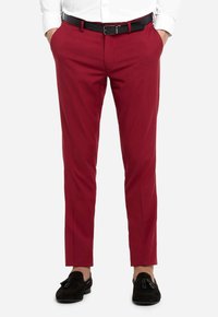 Pantaloni su misura rossi in tessuto liscio, con taglio dritto, passanti per cintura e tasche laterali, abbinati a mocassini neri.