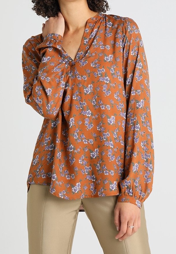 Rustkleurige blouse met een bloemenpatroon in paars en groen, met een v-hals en lange mouwen met gerimpelde manchet.