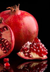 Felrood granaatappel met een gestructureerde buitenkant, opengebroken om glanzende rode zaden te onthullen, rustend op een reflecterende zwarte ondergrond.