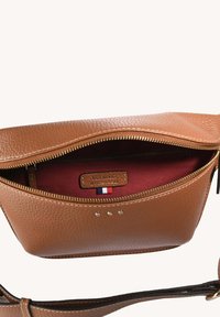 Sac à main en cuir marron avec une surface texturée, fermeture éclair dorée et doublure en tissu rouge. L'étiquette intérieure présente un accent tricolore.