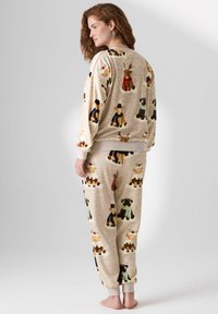 Naine seisab paljajalu beežides mugavates ööriietes, millel on pidulikud koera ja põhjapõdra mustrid, ja vaatab küljele lihtsa tausta ees.