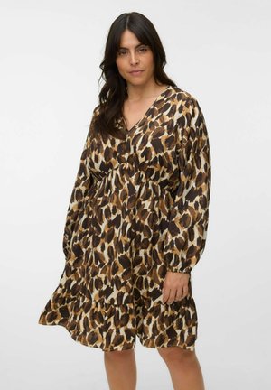 Donna con capelli lunghi e scuri che indossa un abito largo, a manica lunga, al ginocchio con fantasia leopardata marrone e nera.