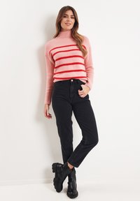 Maglione rosa con strisce rosse, colletto a lupetto e polsini a coste, abbinato a jeans neri a vita alta e stivaletti neri.