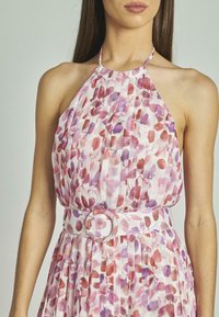 Vestido con cuello halter en tejido ligero con un estampado floral en tonos rosa y púrpura, que presenta pliegues y un detalle de cinturón circular en la cintura.