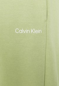 Light green cotton fabric with a smooth texture, featuring a white "Calvin Klein" logo printed on the front. Simple and minimalistic design.