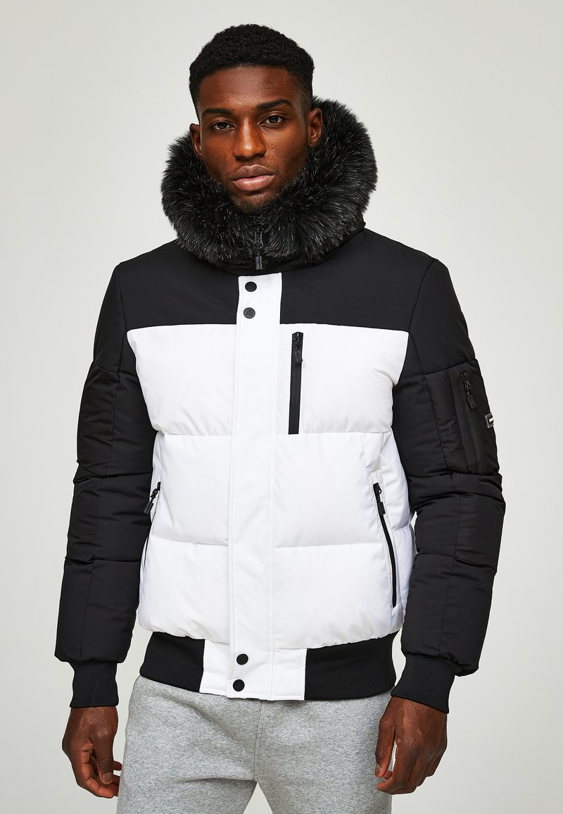 Padded jacket with a black top and white bottom, featuring a faux fur collar, zippered pockets, and button closures. Elasticized waist.