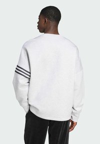 Gray sweatshirt with long sleeves, ribbed crew neck, and three horizontal black stripes on left sleeve. Soft texture and relaxed fit.