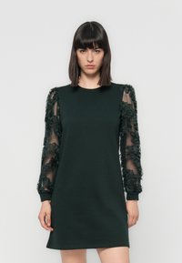 Dark green dress with a crew neck and long sheer sleeves adorned with textured floral appliqués. Fabric is smooth with a relaxed fit.