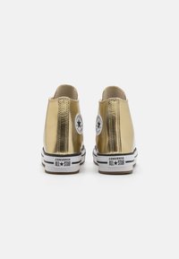 Zlatni metalni Converse All Star tenisice s crno-bijelim prugastim đonom. Sadrže ikonični logo zvijezde na peti i glatku, sjajnu teksturu.