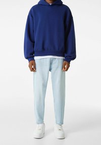 Blå hoodie med känguruficka, i kombination med ljusblå jeans och vita sneakers. Hoodien har en avslappnad passform och ribbade ärmslut.