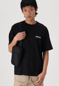Sort bomulds T-shirt med "CREATIVE DEPT" logo, parret med en lille sort crossbody taske med lynlås og et slankt design.