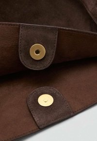 Braunes Wildlederinterieur mit goldenen metallischen Druckknöpfen, ausgestattet mit glatter Textur und sauberem Nähen. Das Design ist minimalistisch und funktional.