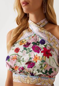 Květinový crop top z saténu s živými duhovými květinami na světle růžovém pozadí, s přiléhavým pasem a křížovým designem popruhů.