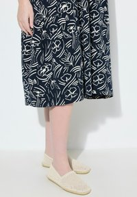 Laivastonsininen mekko, jossa on valkoinen kukkakuvio, polvipituinen, yhdistettynä kermavärisiin liukuviin kenkiin, joissa on kudottu pinta.