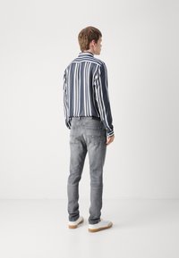 Camisa de manga larga a rayas en azul marino y blanco, combinada con jeans gris claro y zapatillas blancas. Tejido suave, corte ajustado y diseño clásico.