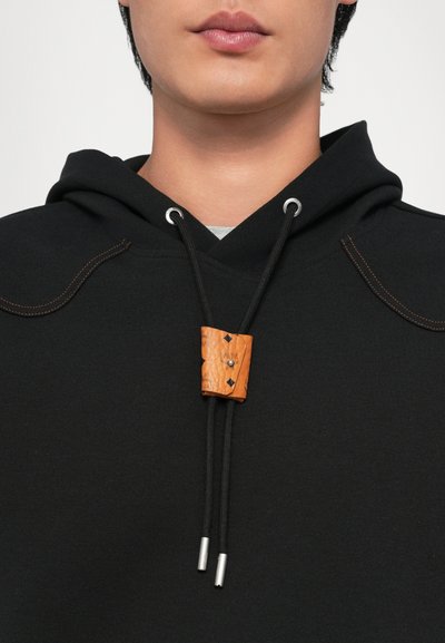 Felpa nera con cappuccio e lacci, caratterizzata da un toggle rettangolare in legno arancione e punte in argento. Le cuciture sui lati delle spalle aggiungono una texture interessante.