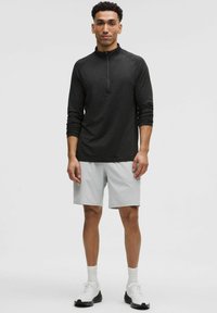 Juodas ilgomis rankovėmis puošnus marškinėliai su ketvirtine užtrauktuku, derinami su šviesiai pilkais šortais. Marškiniai turi tekstūruotą audinį, o šortai pasižymi sklandžiu paviršiumi. Aprangą užbaigia balti sportbačiai.