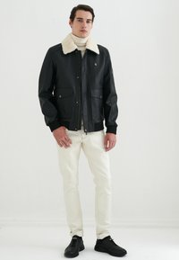 Svart läder bomberjacka med en krämfärgad fuskpälskrage, dragkedja fram och två framfickor, i kombination med vita jeans och svarta sneakers.