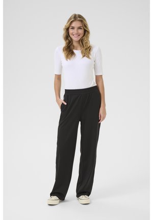 Zwarte sportbroek met een elastische tailleband en zijzakken; gecombineerd met een aansluitend wit T-shirt met korte mouwen en lichtgekleurde sneakers.