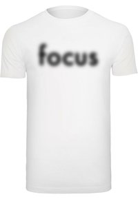 Bijela pamučna majica kratkih rukava s natpisom "focus" u zamagljenom crnom fontu preko prsiju. Jednostavan, neukrašen dizajn.