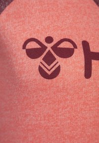 La tela coral presenta un gráfico de abeja marrón con formas simples: dos alas, un cuerpo y patrones de cola, sobre un fondo texturizado.
