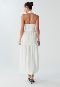 Vestido maxi blanco con cuello halter, con un cuerpo ajustado y falda en capas. Textura suave, cierre de cremallera en la espalda y detalles de diseño minimalistas.