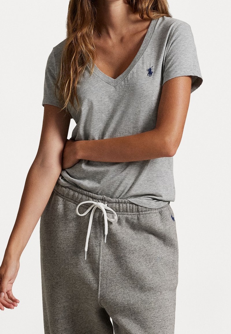 Szara bawełniana koszulka z dekoltem w serek, krótkimi rękawami i małym niebieskim logo na piersi, zestawiona z szarymi spodniami dresowymi ze ściągaczem.