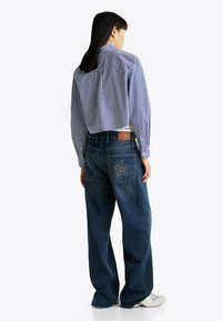 Camisa de manga larga a rayas azules y blancas, combinada con unos vaqueros de corte ancho en azul que presentan un motivo estelar en el bolsillo trasero.
