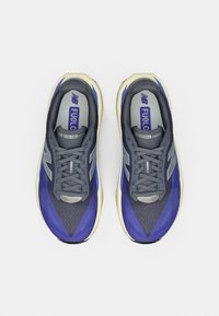 Μπλε και γκρι αθλητικά παπούτσια με υλικά από δίχτυ και καουτσούκ, διαθέτοντας στρογγυλεμένη μύτη, σχέδιο με κορδόνια και έντονη σήμανση "FuelCell".