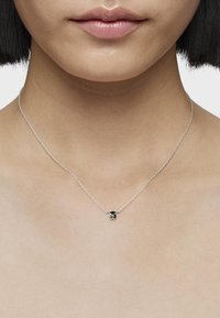 Collana in argento con ciondolo piccolo a forma di cuore in smalto nero, posata su un collo liscio e nudo.