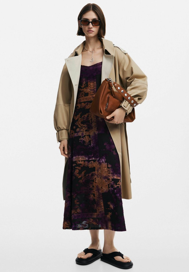 Beiger Trenchcoat über einem lila und schwarzen gemusterten Kleid; braune Tasche mit silbernen Akzenten; schwarze Flip-Flops; dunkle Sonnenbrille; silberne Halskette.