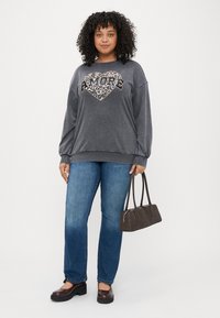 Sweatshirt cinza com um design de coração de leopardo e texto "AMORE", combinado com jeans azuis, sapatos de salto bloco castanhos e uma pequena bolsa castanha.