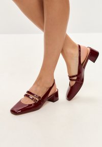 Burgundy lakkbőr szandál sarkú cipők négyzet alakú orral, két pántos díszítéssel és alacsony tömbsarkú stabilitással.