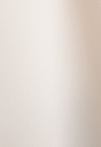 Gros plan d'un tissu lisse beige clair avec une texture subtile et une ombre douce sur toute la surface.