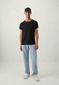 Black short-sleeve t-shirt paired with light blue jeans and white sneakers. The person wears a dark cap and has a neutral expression.