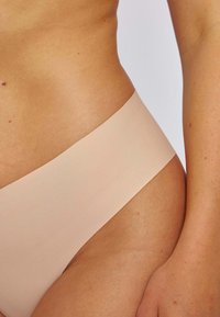 Culotte de bikini nude sans couture avec une texture douce et lisse et une taille large et plate. Design minimal, sans coutures ni motifs visibles.