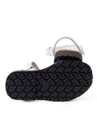 Sandalia blanca con suela de goma negra texturizada, correa ajustable y plantilla de corcho. Acentos metálicos plateados en las correas.