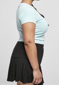 Světlomodré přiléhavé tričko, kombinované s černou plisovanou sukní. Tričko má krátké rukávy; sukně má vrstvu na lemu.