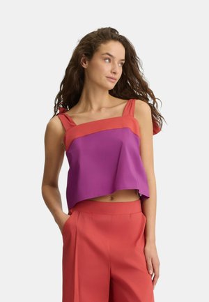 Top senza maniche tagliato con pannelli viola e arancioni, spalline larghe e una texture liscia. Abbinato a pantaloni rossi a vita alta e morbidi.