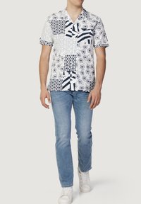 Korte mouwen overhemd in het wit met marineblauwe patronen, waaronder geometrische vormen, cirkels en strepen. Gepaard met lichtblauwe jeans en witte sneakers.