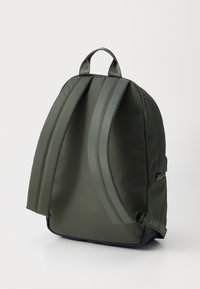 Dark green backpack with a smooth, durable exterior, curved shape, adjustable padded straps, and a contrasting navy base.