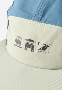 Απαλό πράσινο και μπλε καπέλο με μαύρα τυπωμένα σχέδια, αλεπού με καρύδια, κιάλια με μια κάμπια και πουλί κάτω από φεγγάρι και αστέρια.