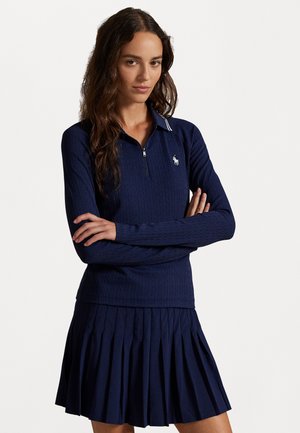 Navy blue knitted zip-up top with a white-collared neckline, paired with a pleated skirt. Features a small logo on the chest.