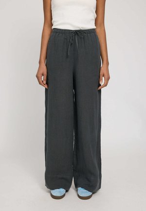 Person wearing loose dark gray wide-leg pants with a drawstring waist and light blue sneakers against a plain background.