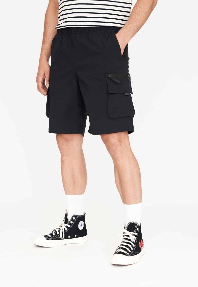 Navyblaue Cargo-Shorts mit elastischem Bund, Seitentaschen und Reißverschlussdetails. Getragen mit schwarzen High-Top-Sneakern und weißen Socken.