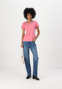 Pink short-sleeve t-shirt with embellished neckline, blue straight-leg jeans, black heeled boots, and a beige handbag.