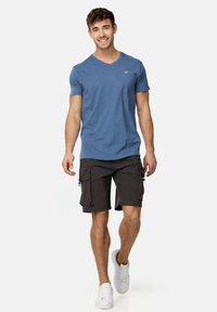 Blå v-hals t-shirt parret med sorte cargo shorts. Shortsene har flere lommer og en glat tekstur, accentueret af lynlåse. Hvide sneakers fuldender looket.