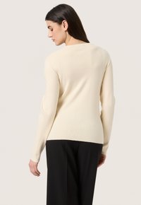 Helles beiges Strickpullover mit tailliertem Design, langen Ärmeln und einfachem Rundhalsausschnitt. Die Rückansicht zeigt eine glatte Textur und dezente Nähdetails.