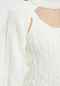 Sweter dziany w kolorze białym z wzorami warkoczowymi, z wyciętymi ramionami, wysokim kołnierzem i teksturowanymi detalami na rękawach.